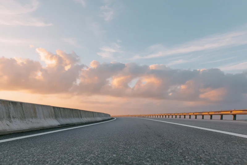 Empty curved asphalt highway sweeping right with guardrails under sunset sky