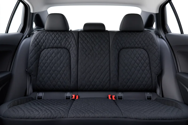 Rear bench seat of a compact car with three seats and quilted black fabric upholstery, isolated against white background
