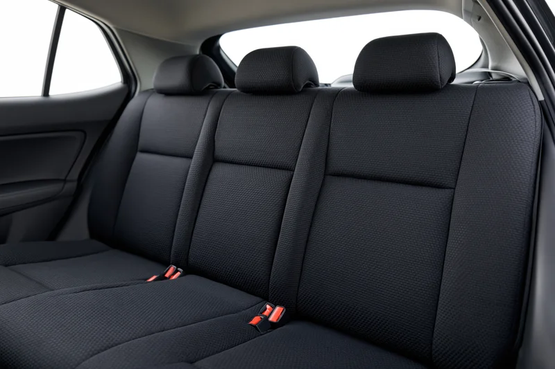 Rear bench seats in a compact car interior with black fabric upholstery and red seatbelt buckles