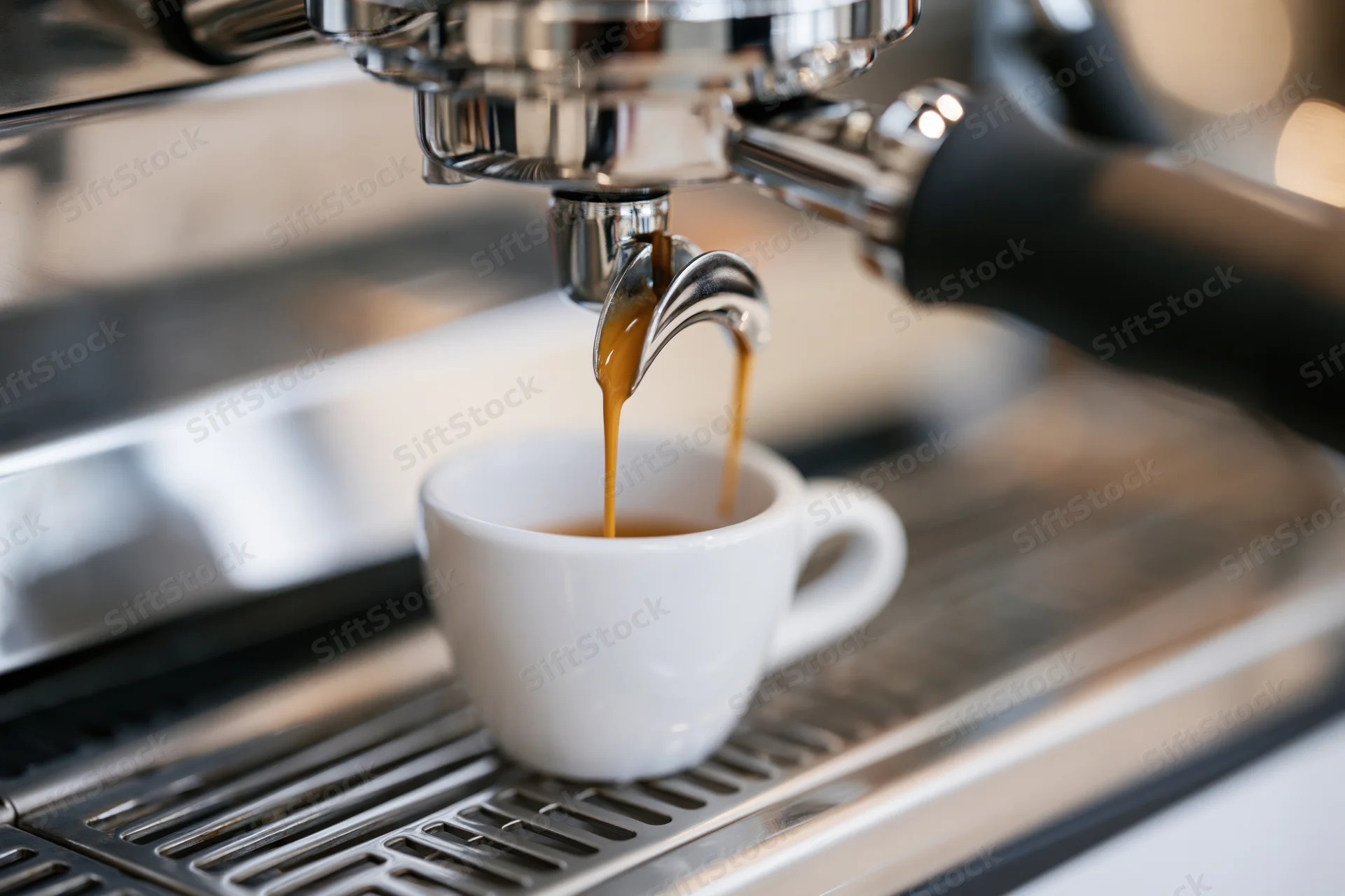 Espresso pouring from chrome portafilter into small white cup on espresso machine drip tray