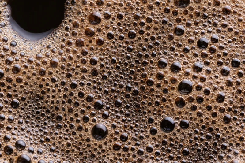 Close-up of black coffee surface covered in fine foam bubbles