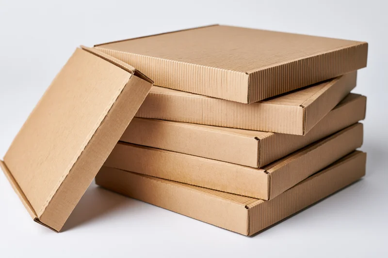 Stack of plain corrugated cardboard pizza boxes with one lid open, arranged vertically on white background