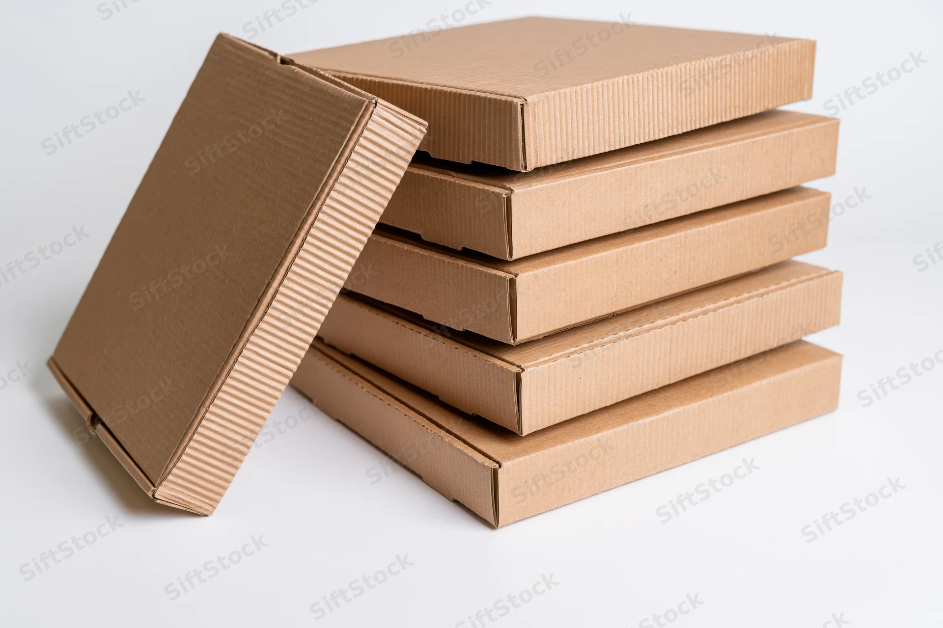 Stack of plain corrugated cardboard pizza boxes with one lid open and leaning against the pile on a white background