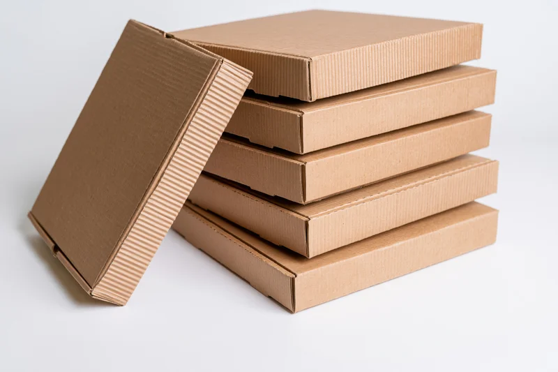 Stack of plain corrugated cardboard pizza boxes with one lid open and leaning against the pile on a white background