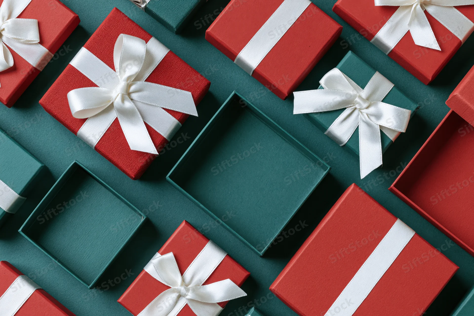Red and dark green gift boxes with white ribbons arranged in a flat lay on a teal surface with copyspace