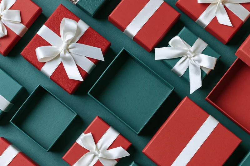 Red and dark green gift boxes with white ribbons arranged in a flat lay on a teal surface with copyspace