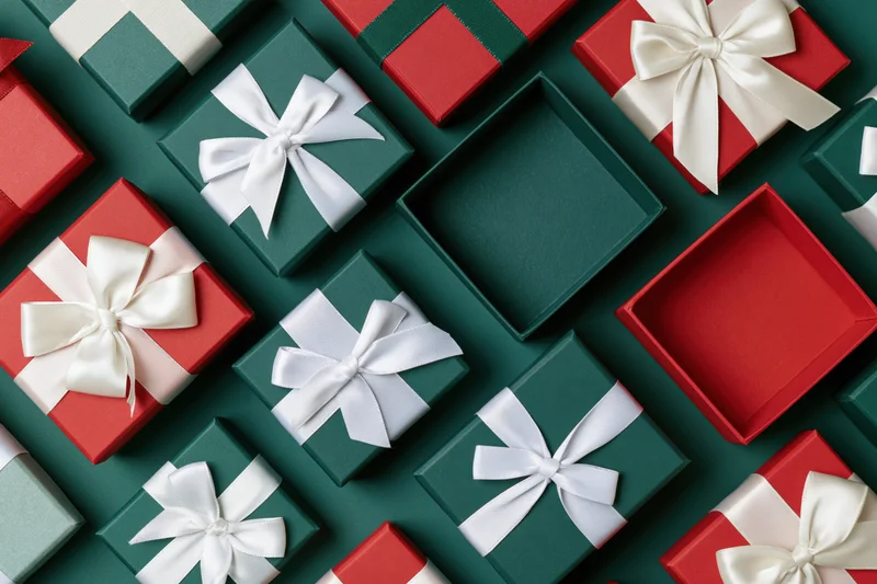 Assorted red and dark green gift boxes with white ribbons arranged in flat lay on dark green surface