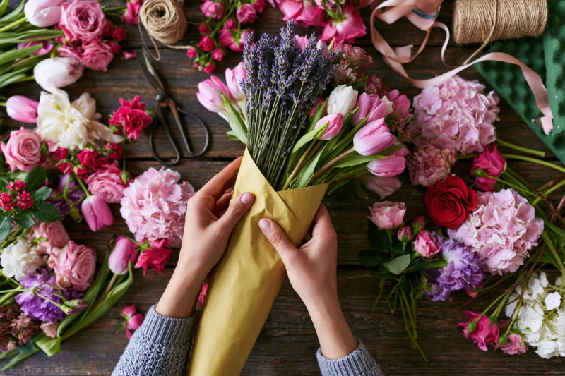 Florist hands wrapping a bouquet in yellow kraft paper on wooden table