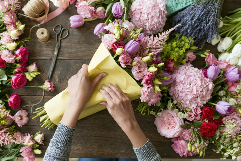 Florist hands wrapping a bouquet in yellow kraft paper on wooden table