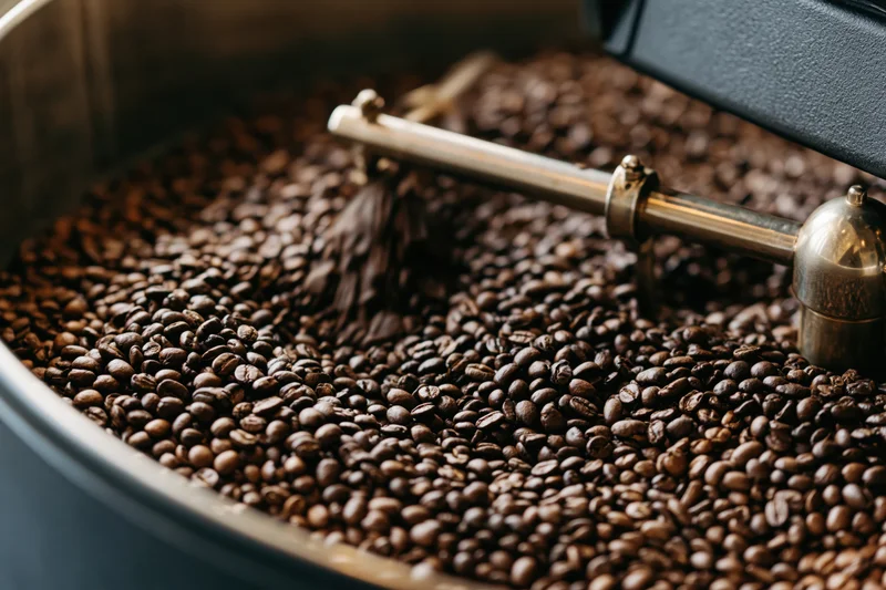 Roasted coffee beans cooling in a large industrial drum with a metal agitator paddle