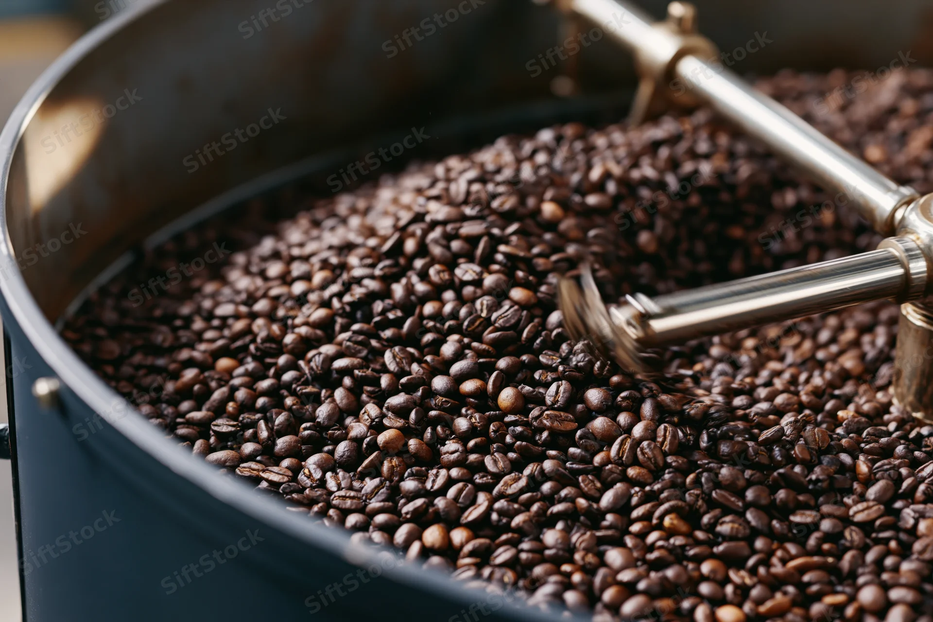 Roasted coffee beans cooling in a large industrial drum with metal stirrers