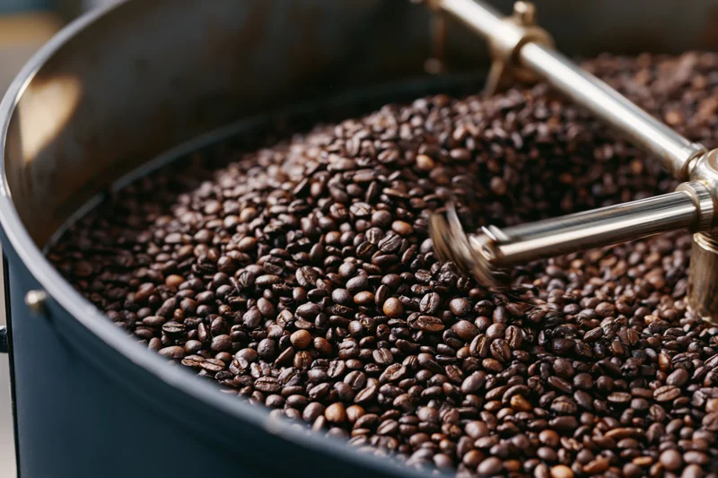 Roasted coffee beans cooling in a large industrial drum with metal stirrers