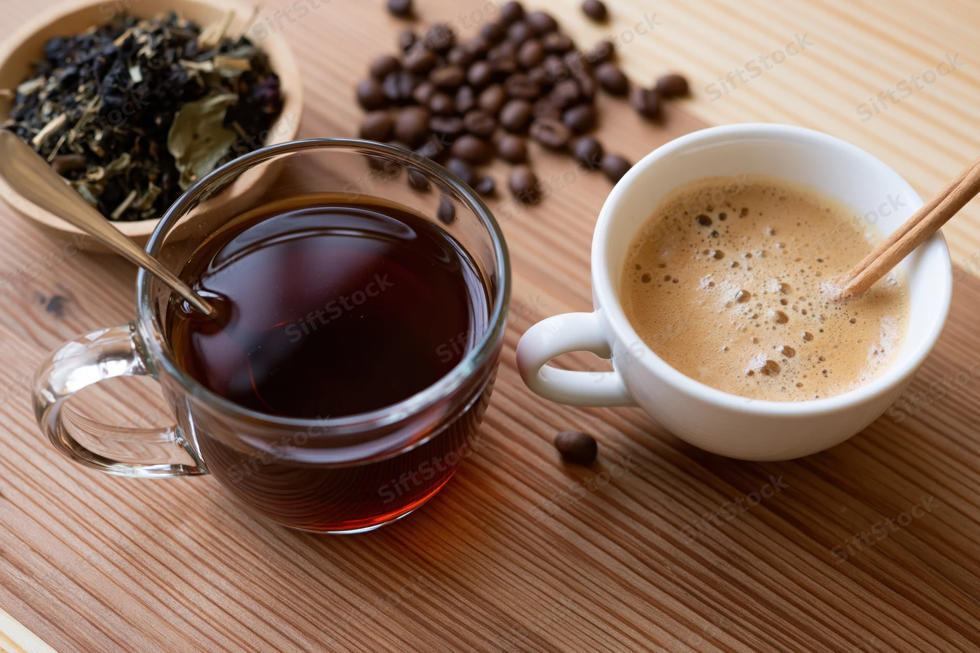 Glass mug of dark tea and white cup of frothy coffee on wooden table with coffee beans and tea leaves nearby