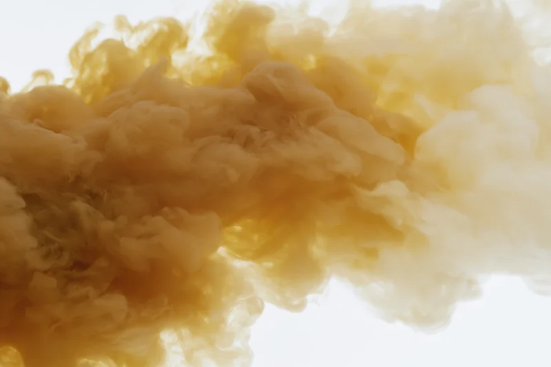 Golden amber ink dispersing in clear water forming swirling clouds against white background