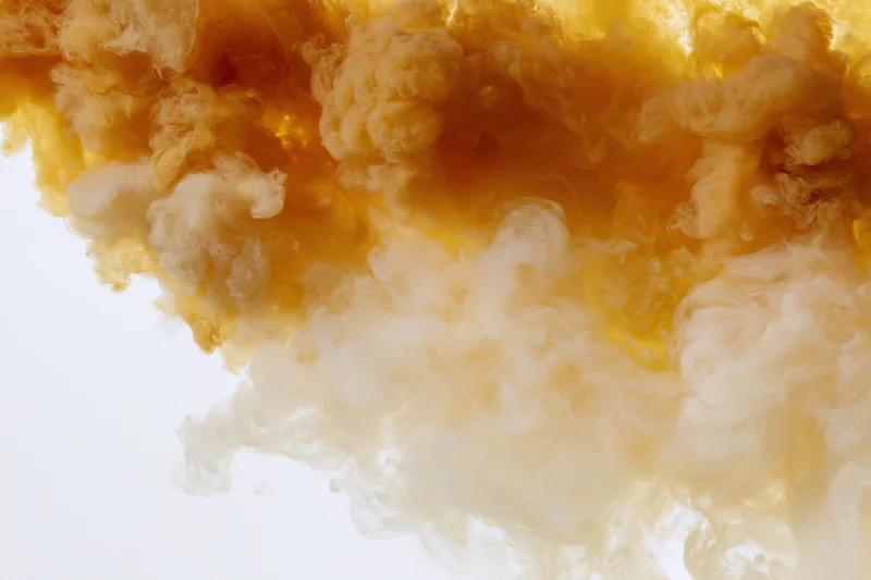 Golden amber ink dispersing in clear water forming swirling clouds against white background