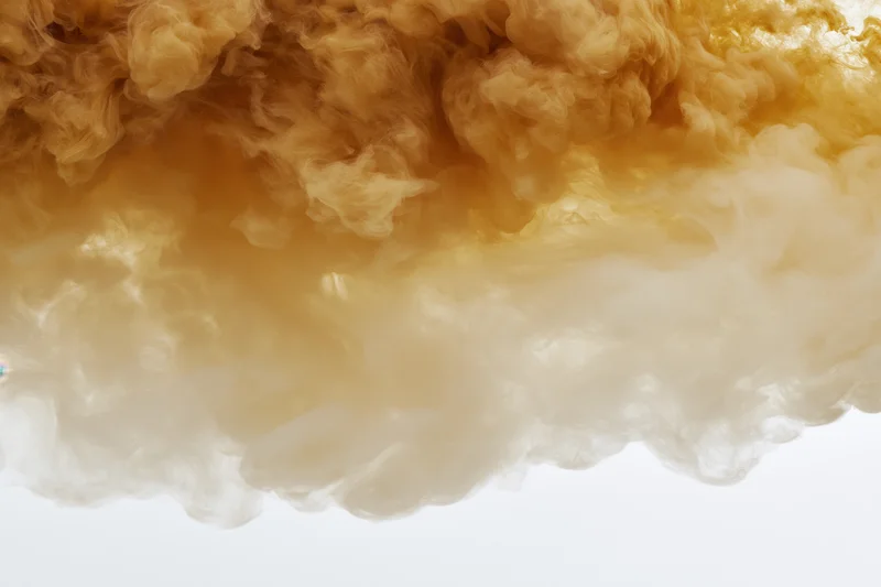 Golden amber ink dispersing in clear water forming swirling clouds against white background
