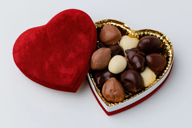 Open heart-shaped red velvet chocolate gift box with assorted chocolates inside on white background