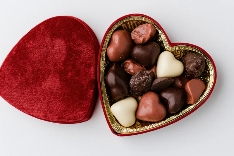 Open heart-shaped red velvet chocolate gift box with assorted chocolates inside on white background