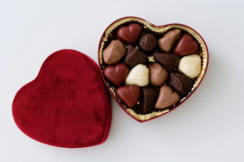 Open heart-shaped red velvet chocolate gift box with assorted chocolates inside on white background