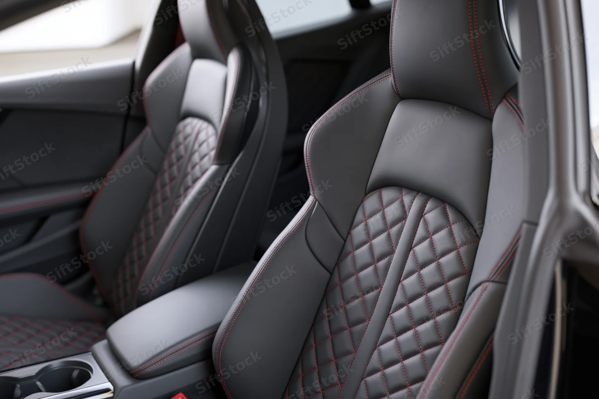 Two black leather sport car seats with diamond stitching and red contrast trim in vehicle interior
