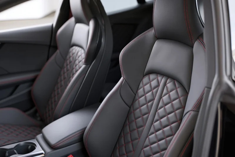 Two black leather sport car seats with diamond stitching and red contrast trim in vehicle interior