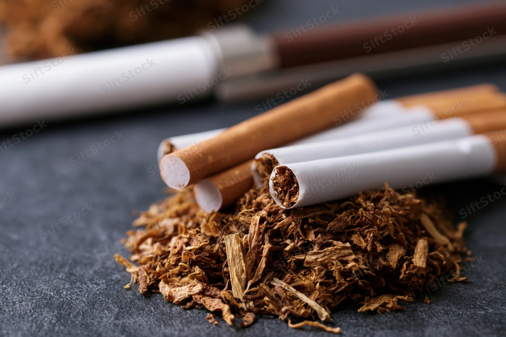 Loose tobacco piled with unfiltered cigarettes arranged on dark surface