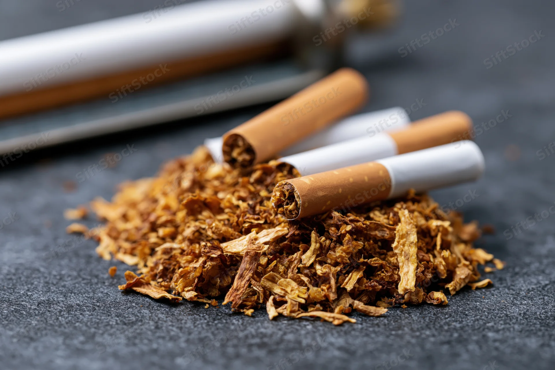 Loose tobacco piled on dark surface with unfiltered cigarettes arranged on top
