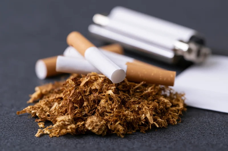 Loose tobacco pile with unfiltered cigarettes and lighter on dark surface