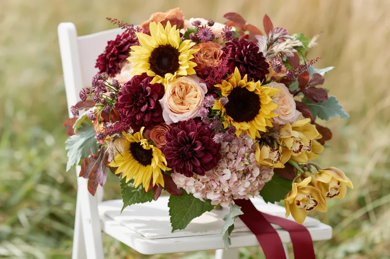 Lush autumn bridal bouquet resting on white wooden chair outdoors