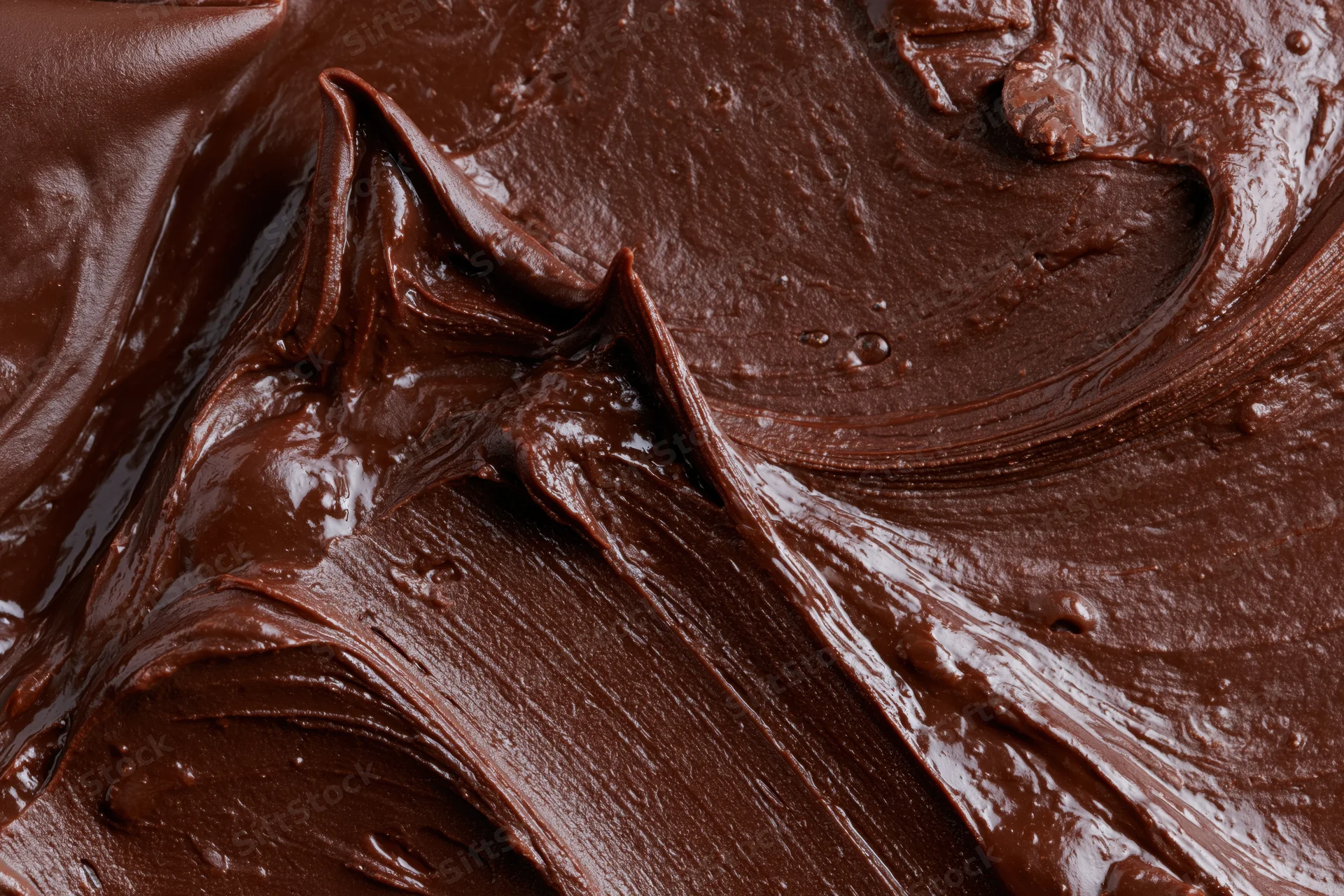 Thick melted dark chocolate spread in swirling texture across flat surface