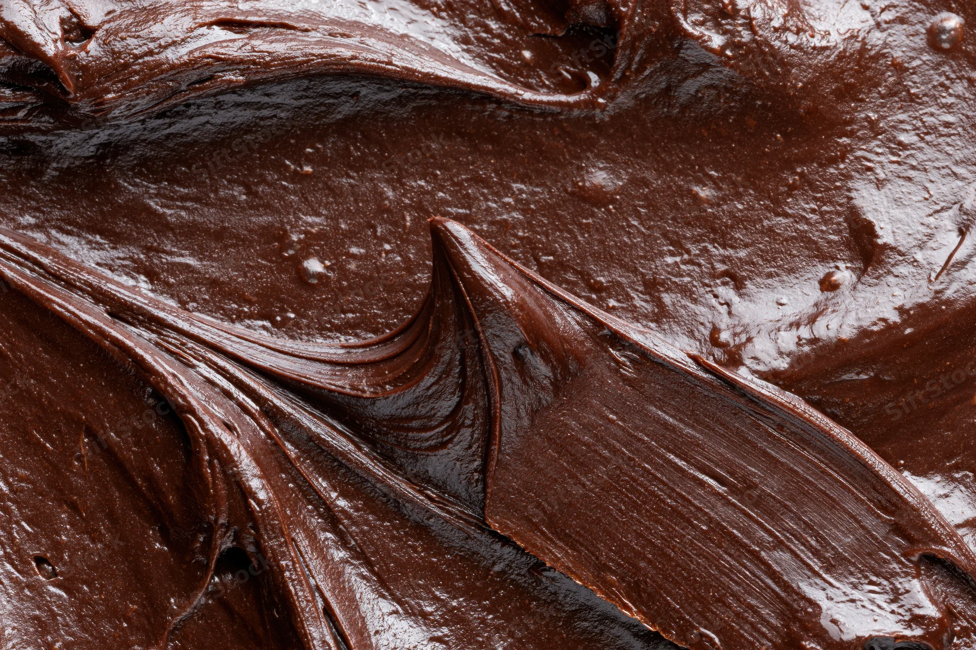 Thick melted dark chocolate spread across a flat surface in glossy swirls