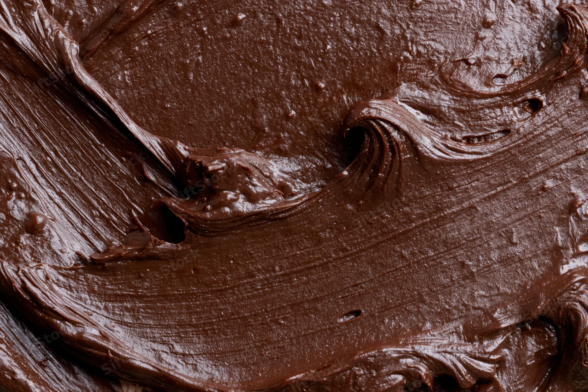 Thick melted dark chocolate spread in swirling patterns across a flat surface