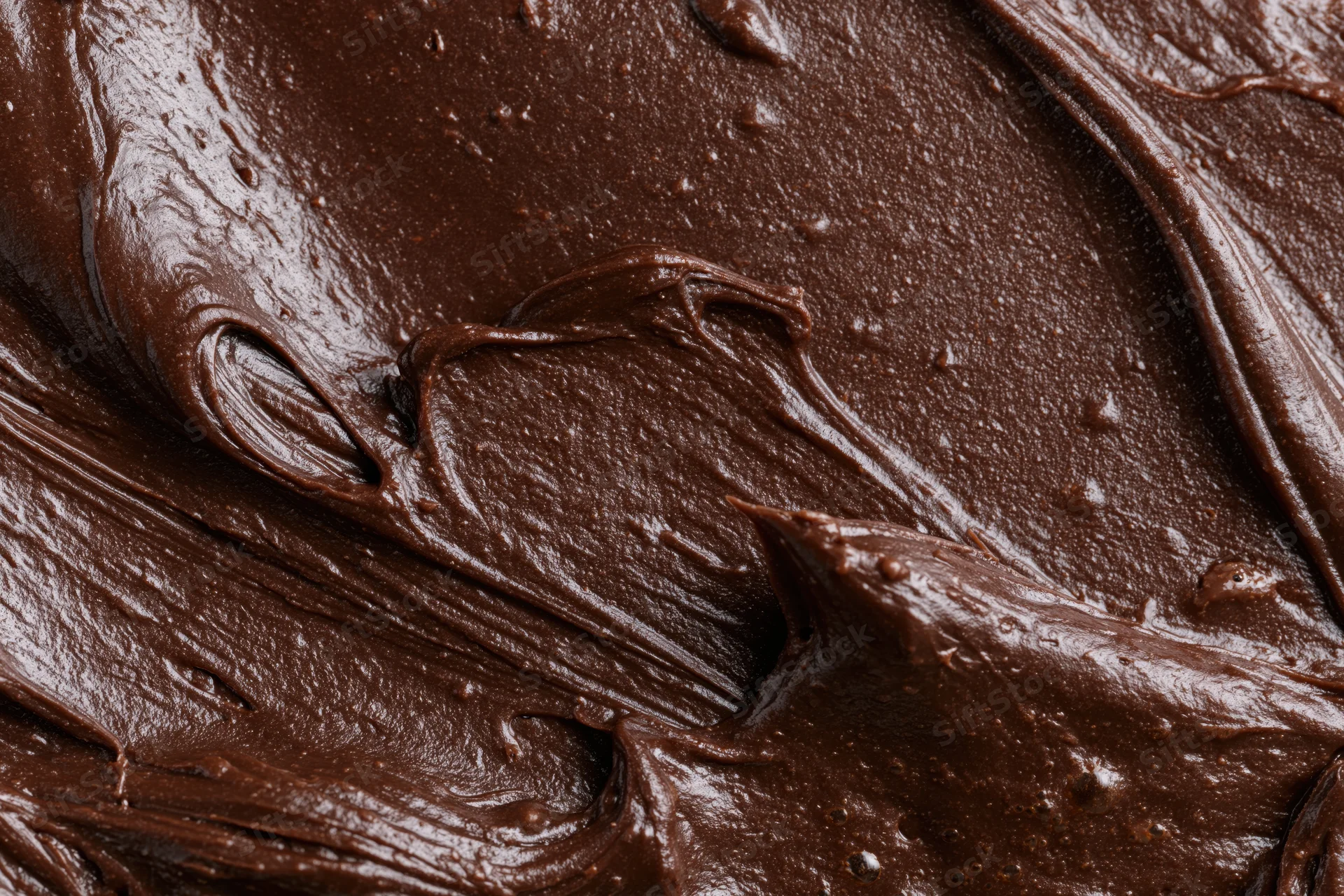 Thick melted dark chocolate spread in glossy swirls across a flat surface