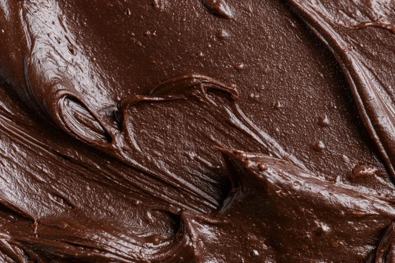 Thick melted dark chocolate spread in glossy swirls across a flat surface