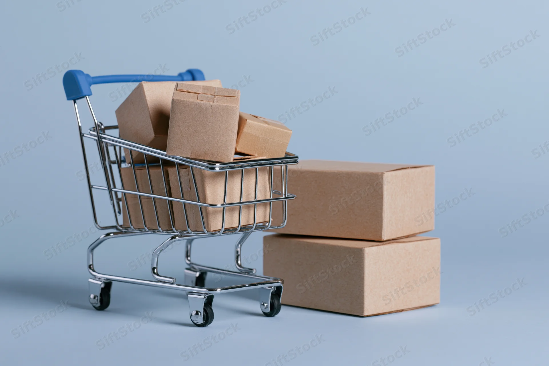 Miniature metal shopping cart filled with small cardboard boxes on a plain surface