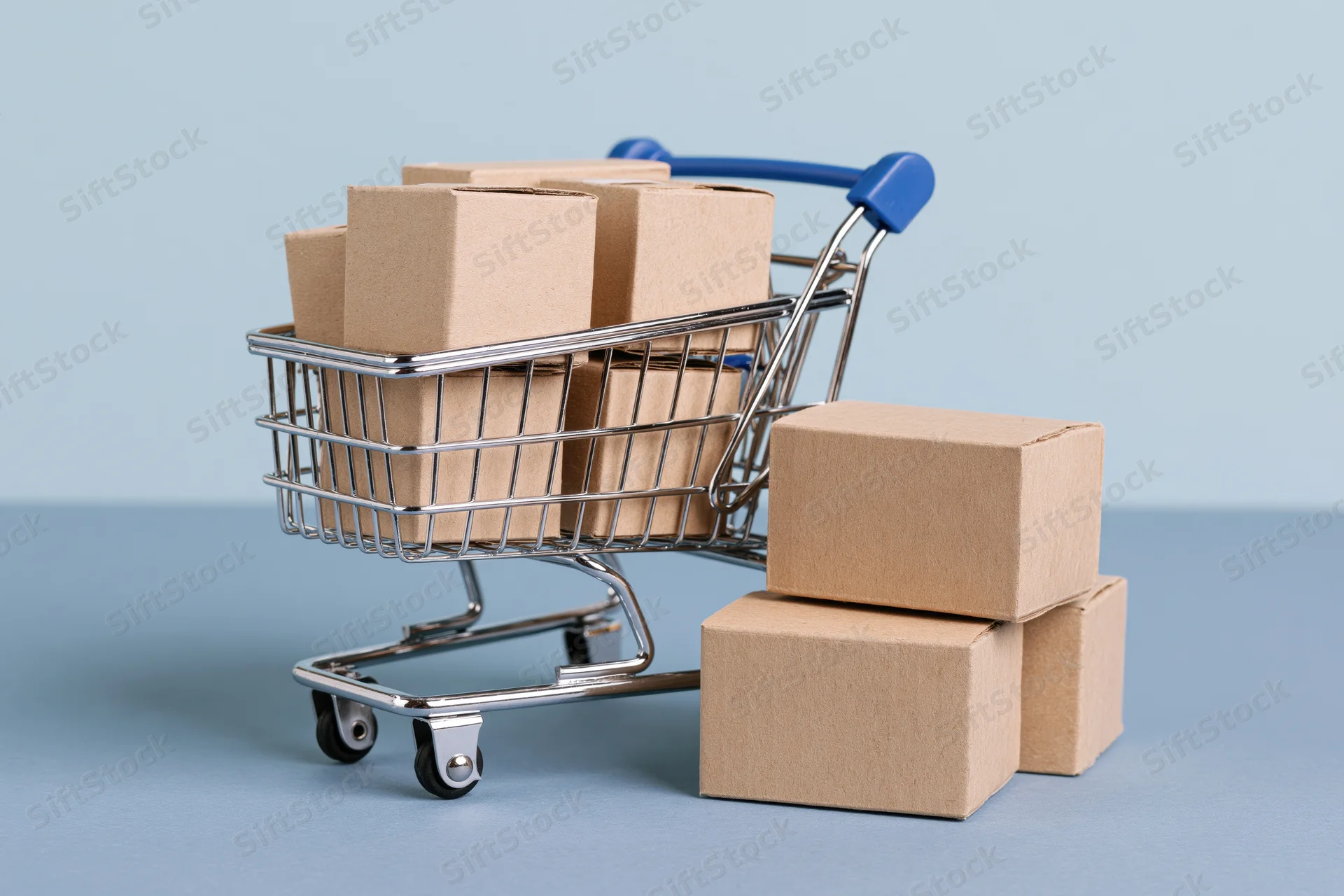Miniature metal shopping cart filled with small cardboard boxes on a blue surface