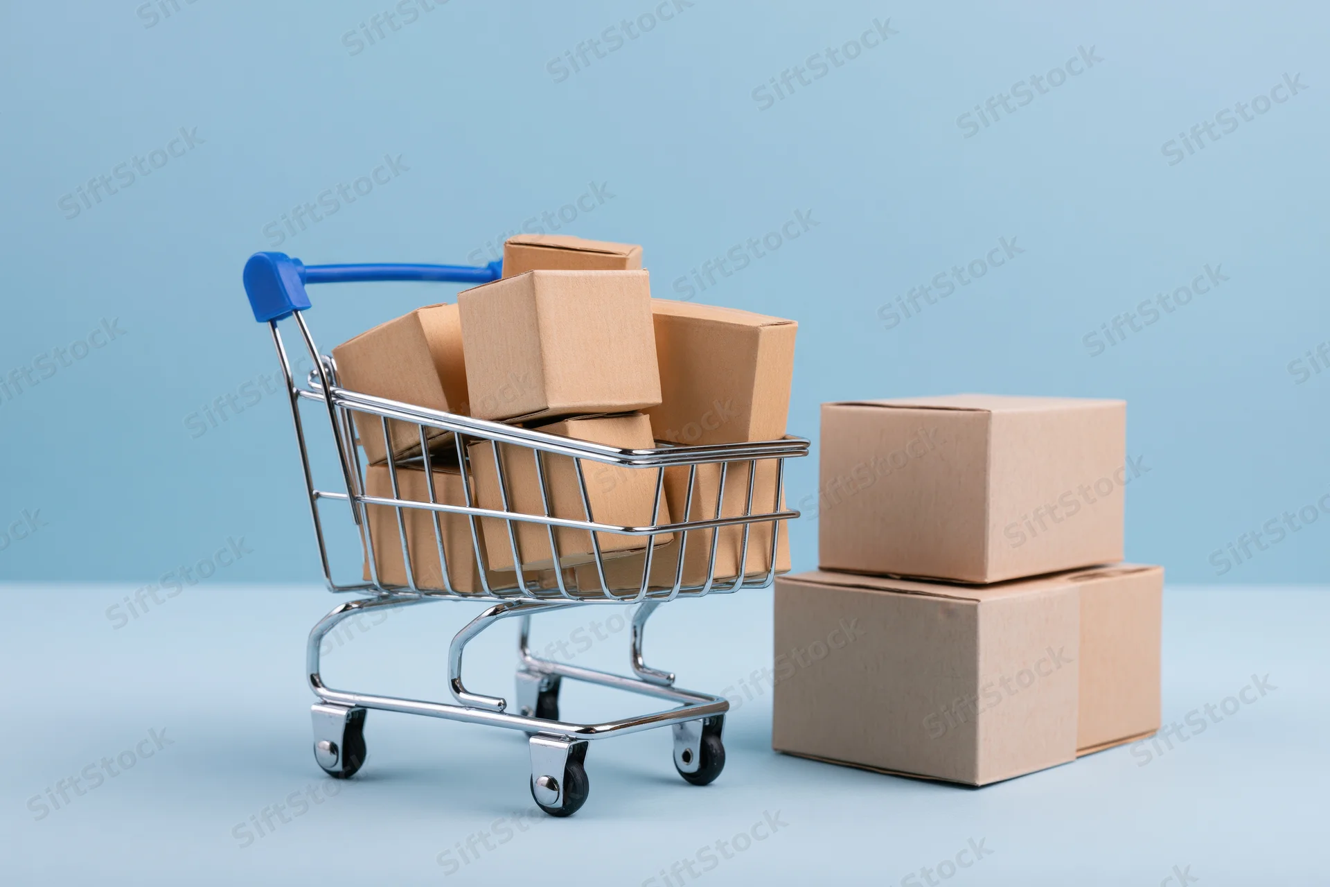 Miniature metal shopping cart filled with small cardboard boxes on a blue surface