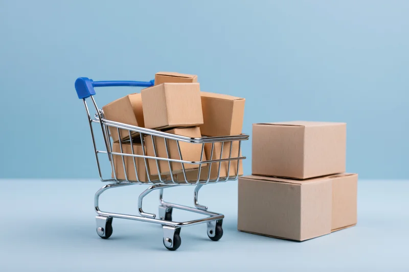 Miniature metal shopping cart filled with small cardboard boxes on a blue surface