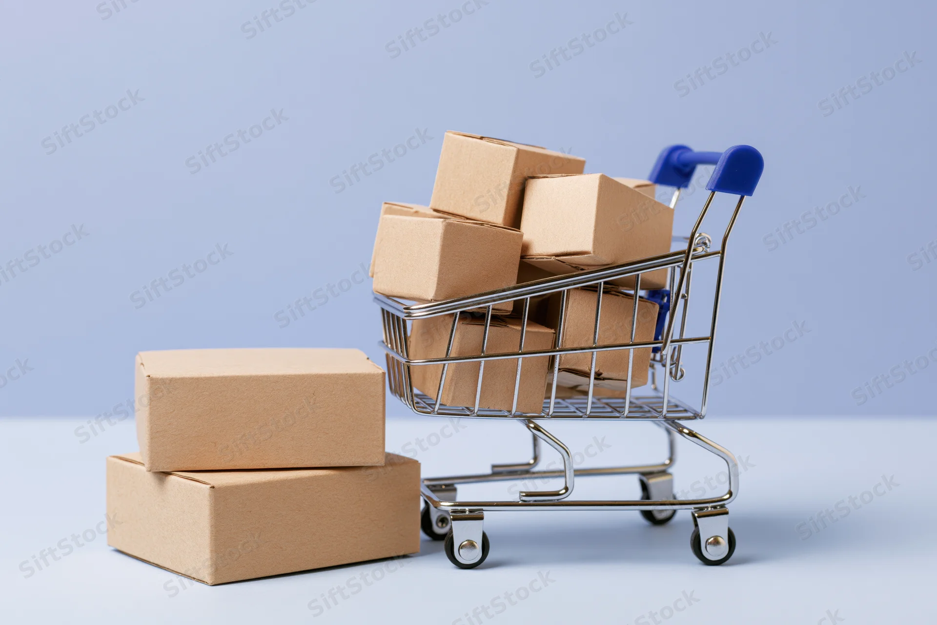 Miniature metal shopping cart filled with small cardboard boxes on a plain surface