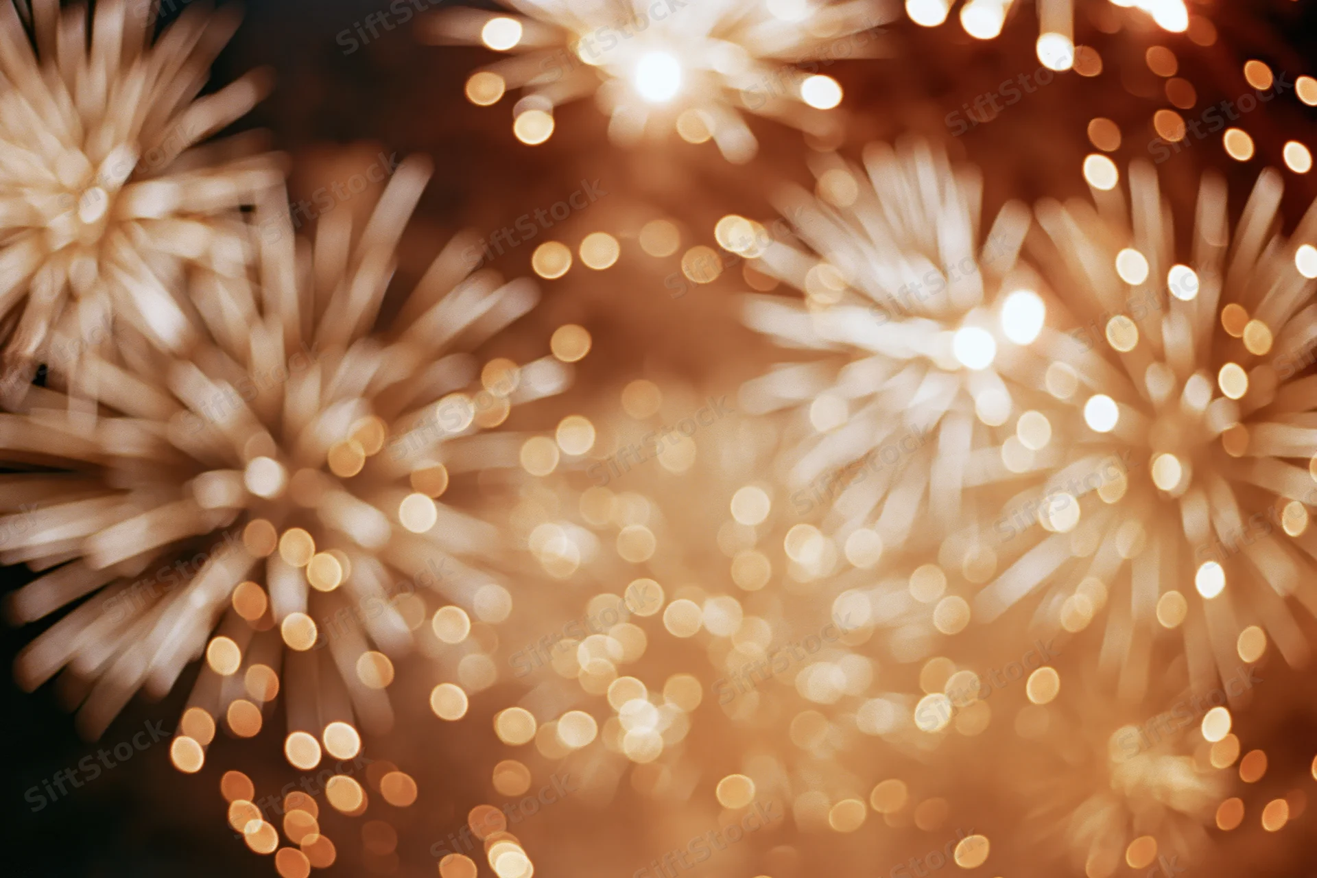 Fireworks bursting across night sky in abstract bokeh pattern with warm golden glow