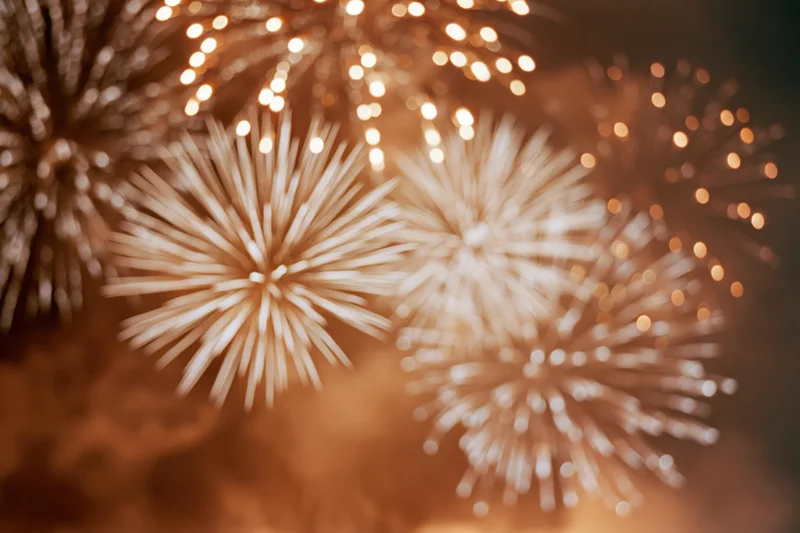 Fireworks bursting across night sky in warm golden light with bokeh effect