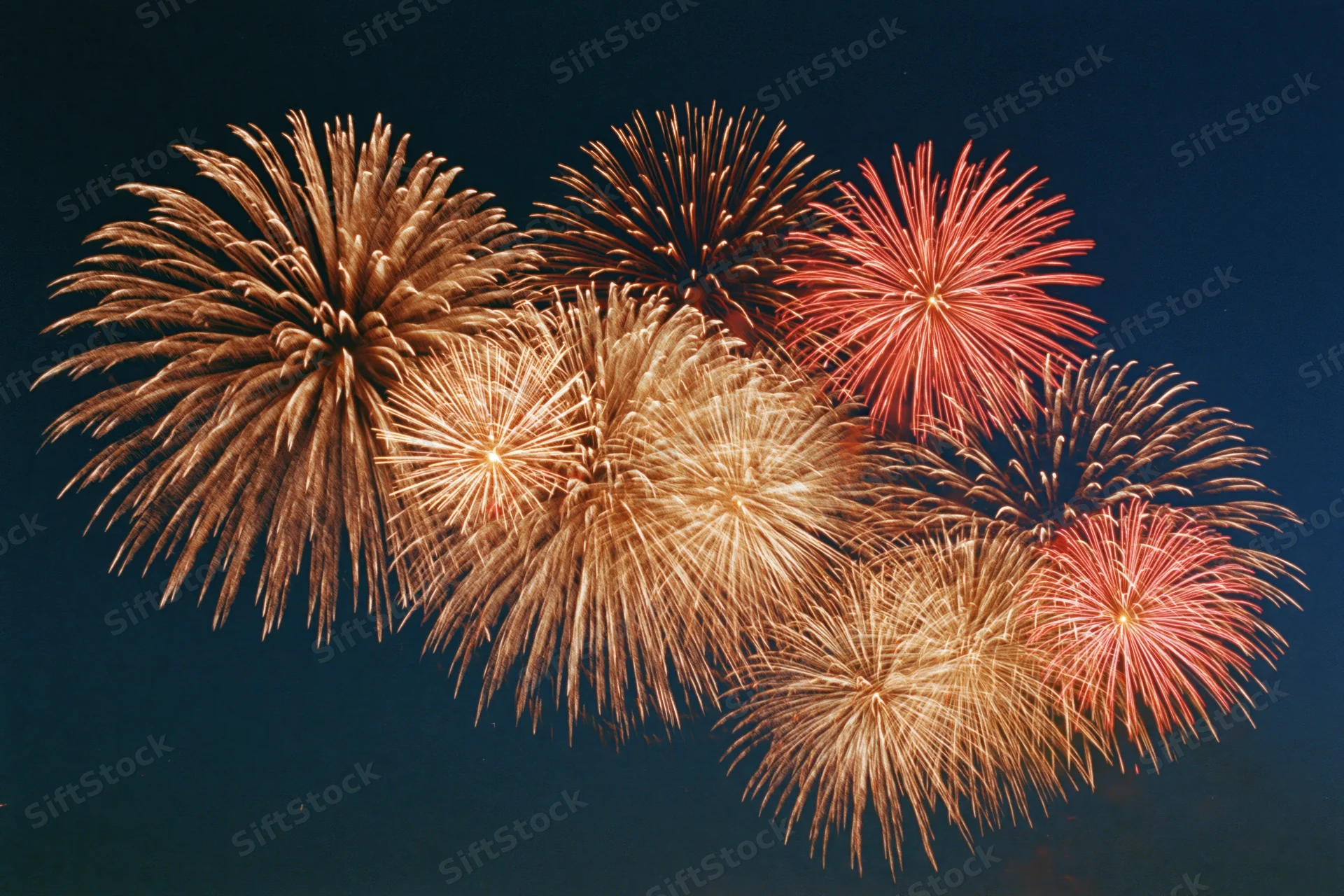 Multiple fireworks bursting simultaneously across the night sky
