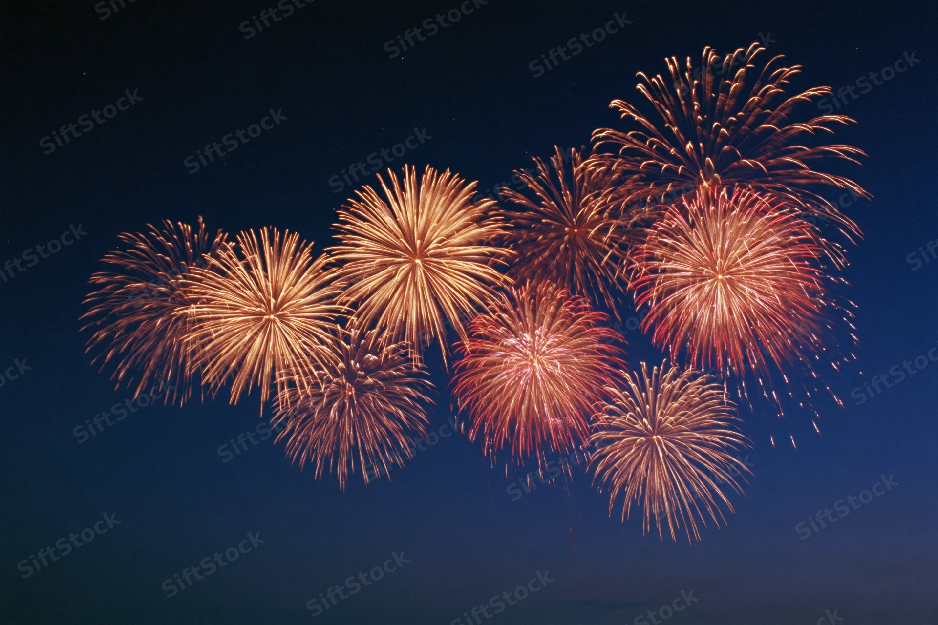Multiple fireworks bursting simultaneously across the upper night sky