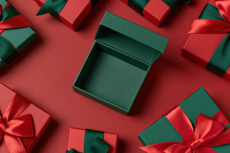 Open green gift box centered and empty surrounded by wrapped presents on red background