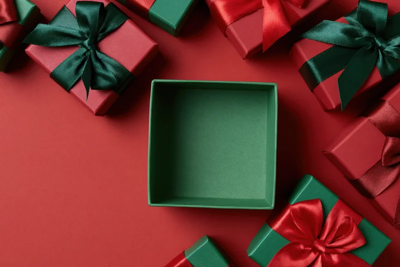 Open green gift box centered and empty surrounded by wrapped presents on red surface