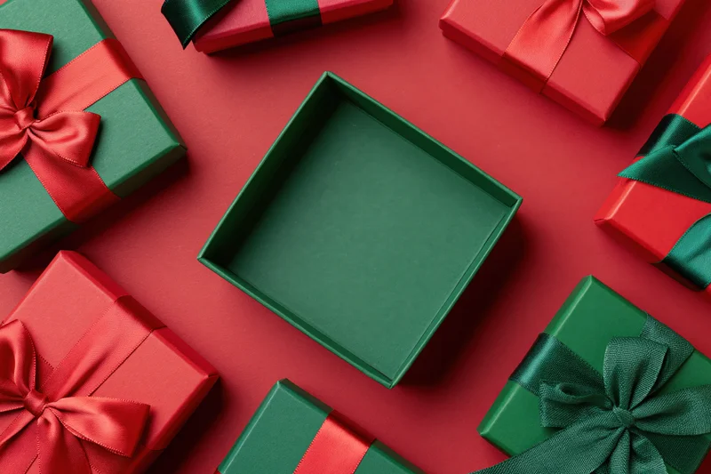 Open green gift box centered and empty surrounded by wrapped presents on red surface