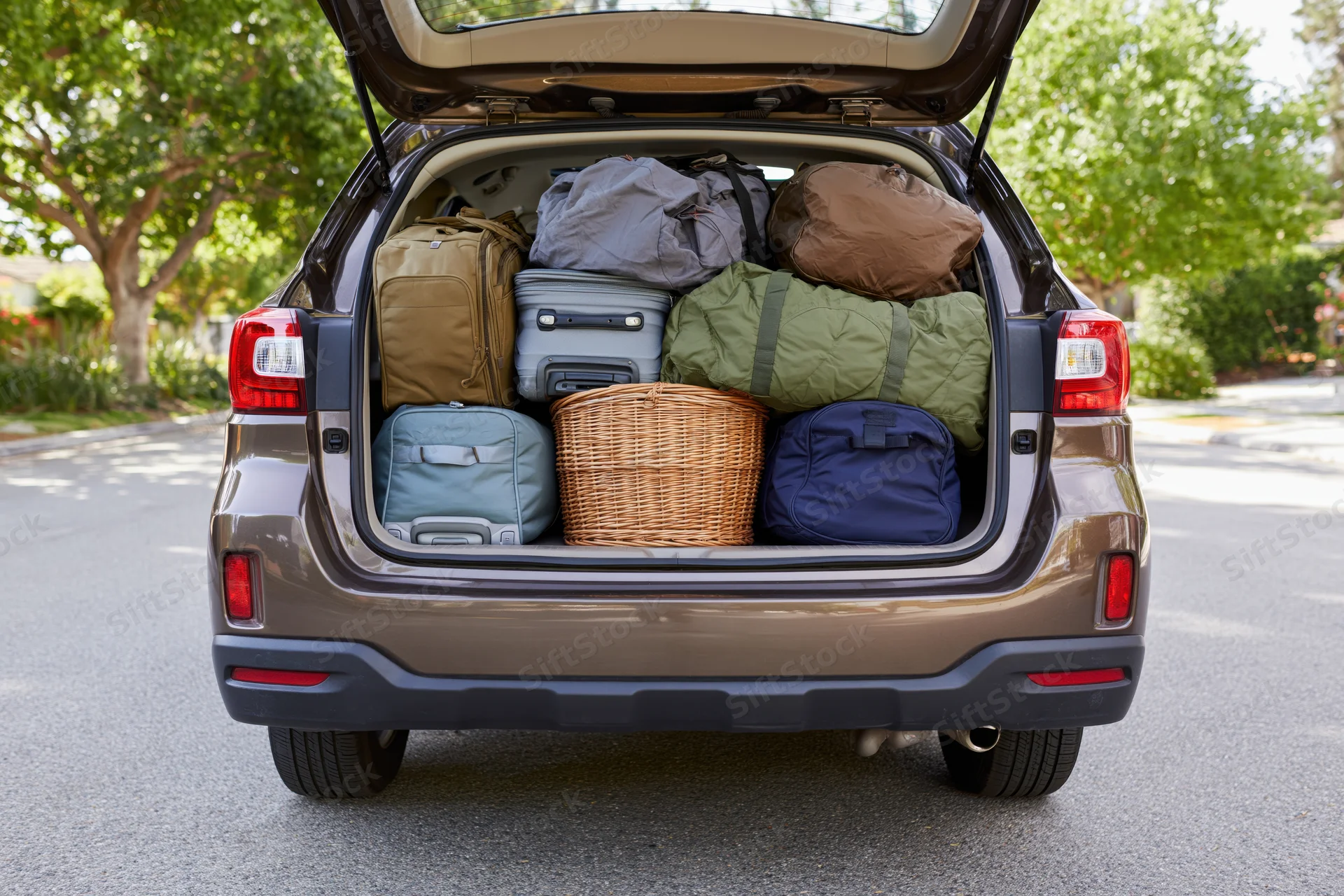 Open trunk of dark bronze suv packed with luggage and bags on residential street
