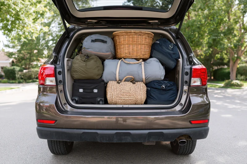 Open trunk of dark bronze suv packed with luggage and baskets in suburban driveway
