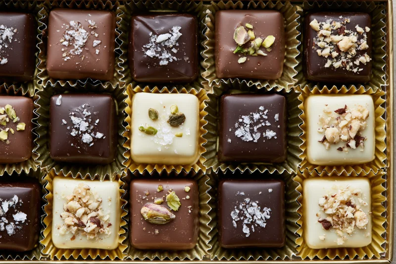 Assorted square chocolates arranged in a gold-lined box with various toppings and wrappers