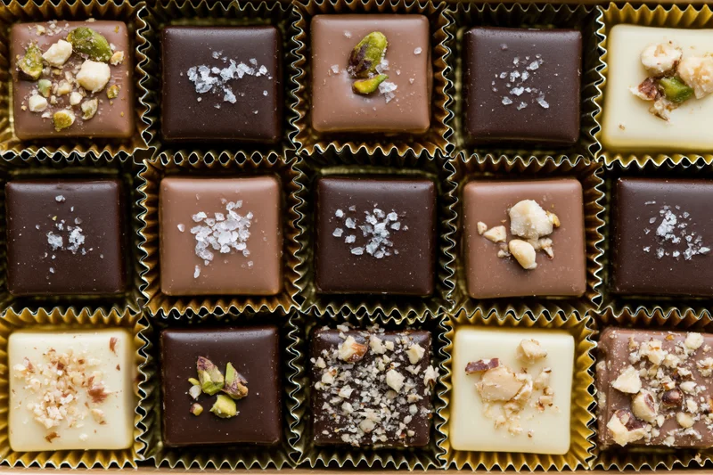 Overhead close-up of assorted square chocolates arranged in a grid inside a box with gold foil wrappers